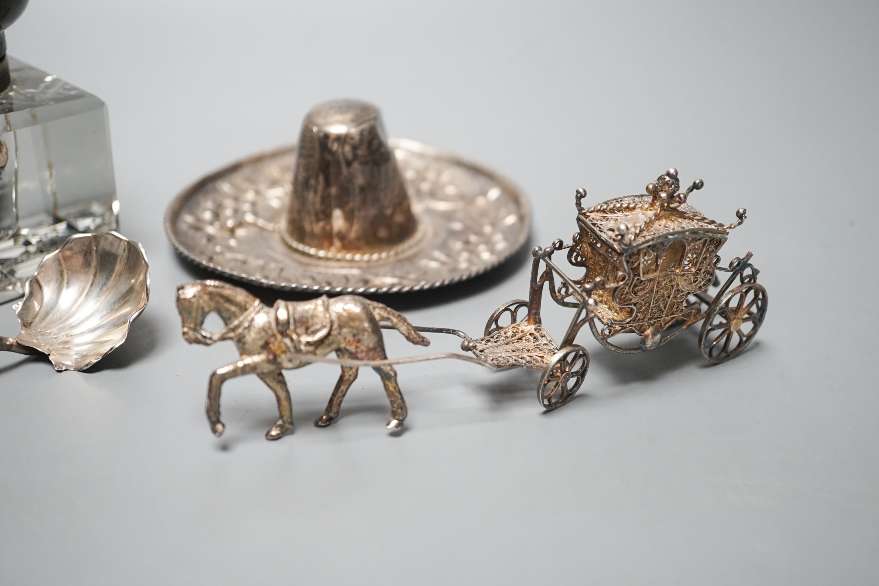 A silver mounted glass inkwell, A Mexican white metal miniature sombrero, a white metal caddy spoon and a filigree horse and carriage.